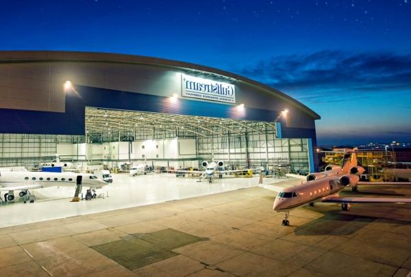 Exterior of Gulf Stream Service Center at night. Planes inside hangar and outside on apron.